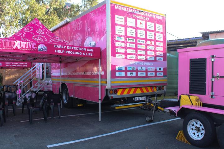 A pink PinkDrive mobile mammography unit parked with its awning up for a breast screening day, its side reading “Early detection can help prolong a life”.