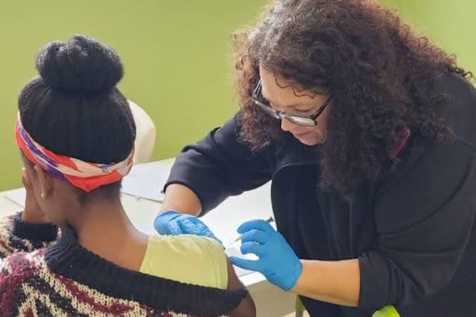 A gloved nurse gives a schoolgirl an injection in her upper arm at a school vaccination session.