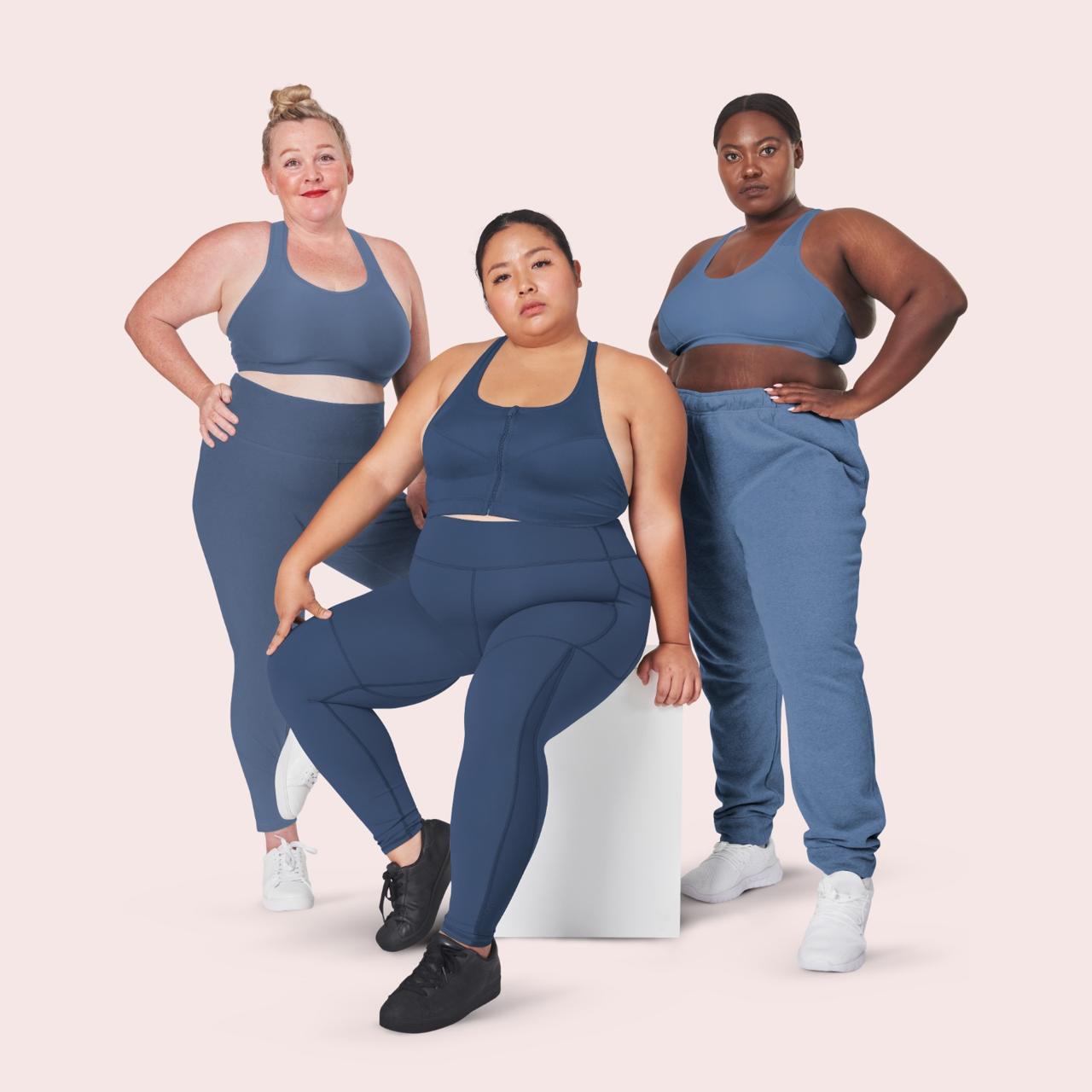 Three plus-size women in matching blue activewear standing together against a pink backdrop.