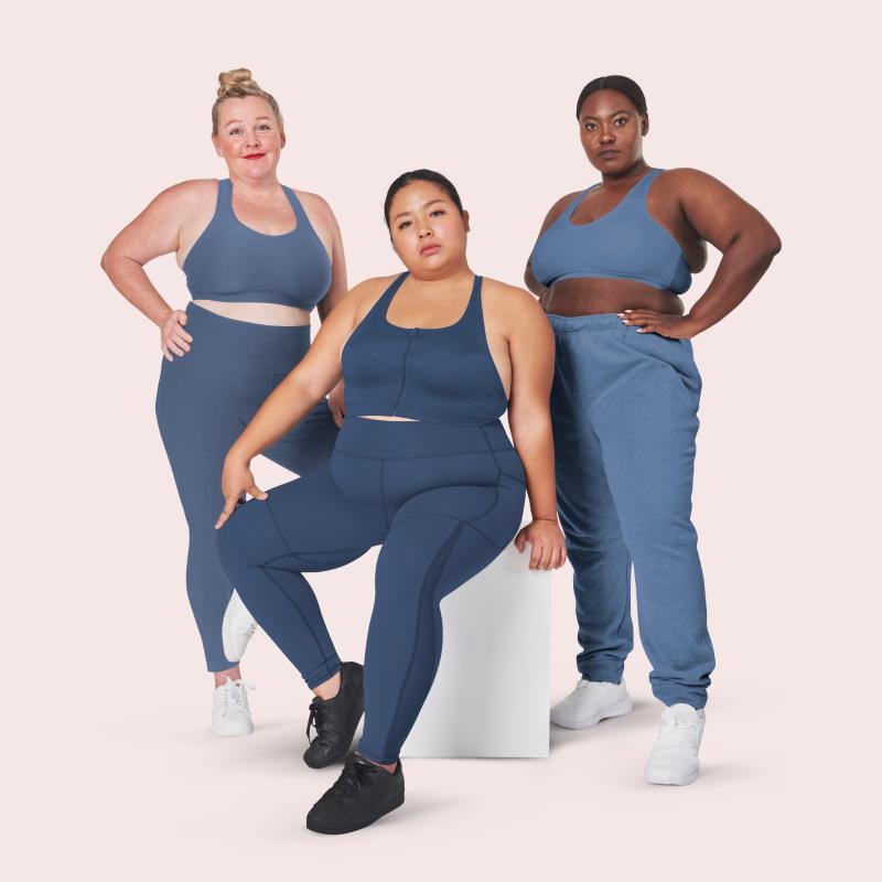 Three plus-size women in matching blue activewear standing together against a pink backdrop.