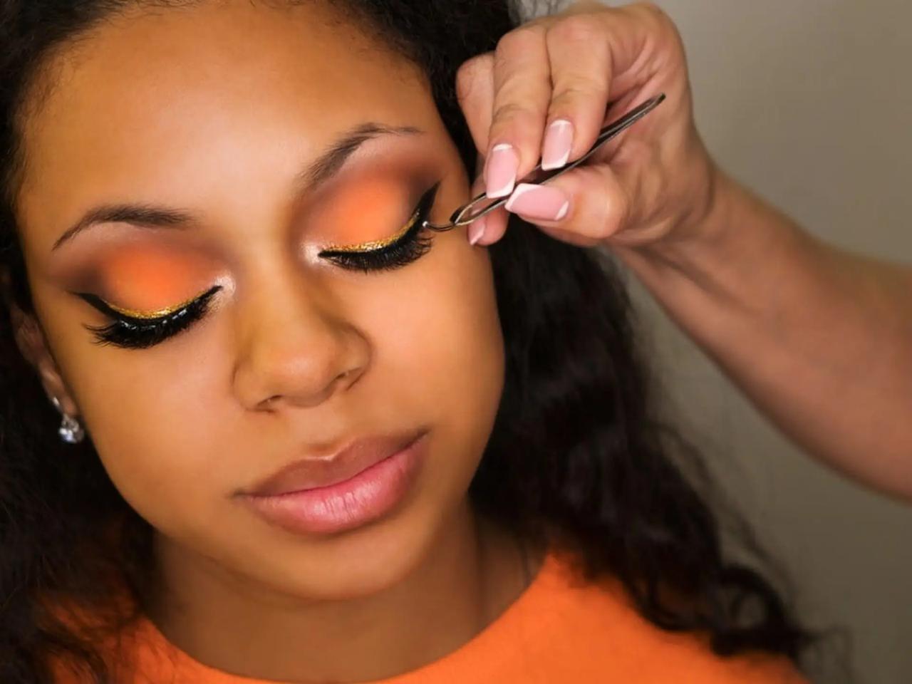 A close-up of a young woman’s closed eye as a technician applies a lash strip with tweezers.